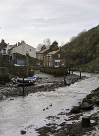 Houses by river and buildings against sky