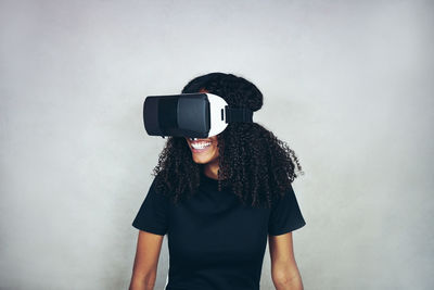 Smiling woman wearing virtual reality simulator while standing against wall