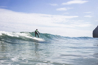 Rear view of surfer surfing in sea against sky