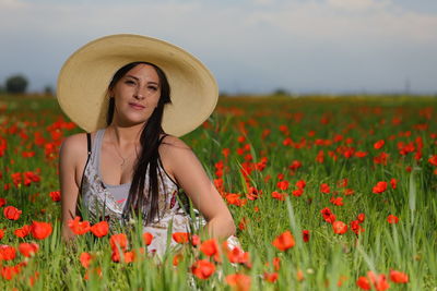 Portrait of young woman sitting amidst poppy flowers on field