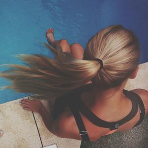 Full length rear view of woman sitting by swimming pool