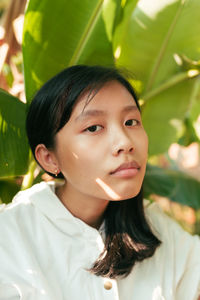 Close-up portrait of young woman against leaves