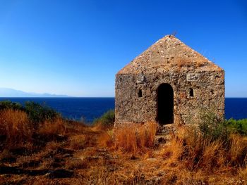 Old ruin by sea against clear blue sky