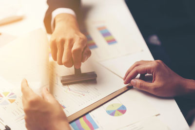 Midsection of business colleague applying rubber stamp on graphs