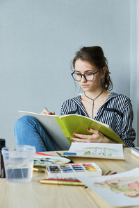 Millennial girl draws fabulous images on paper while sitting at home