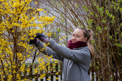 Side view of young woman trimming bushes in the spring garden.