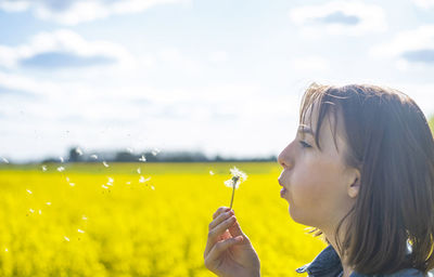 Portrait of young woman with yellow dandelion on field