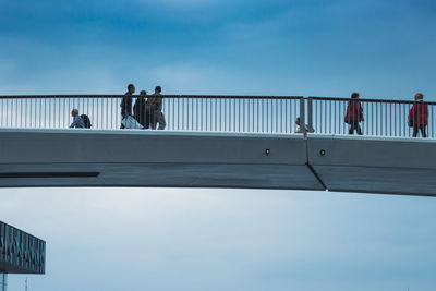 People walking on footbridge against sky