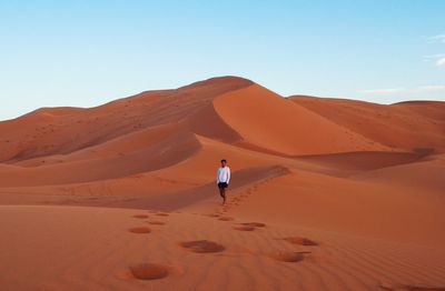Man walking on sand dune at sahara desert against sky