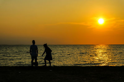 Silhouette people on beach against orange sky