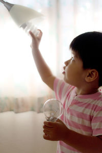 Cute boy replacing light bulb with energy efficient lightbulb in lamp at home