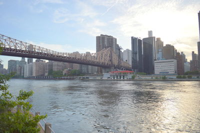 Bridge over river by buildings against sky in city