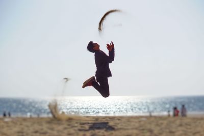 Full length of man jumping at beach against sky