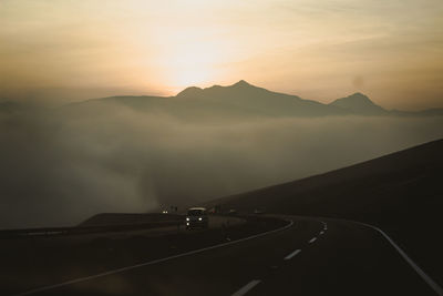 Road by mountains against sky during sunset