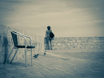 Rear view of man standing on chair against sky