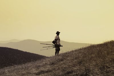 Man holding tripod and camera while standing on field at mountain during sunset