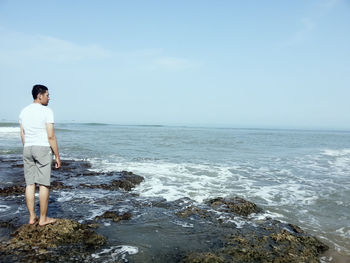 Man standing on rock in sea against sky