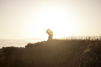 Silhouette couple kissing while standing on field against clear sky during sunset