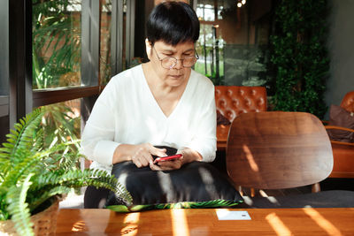 Woman holding mobile phone while sitting on table