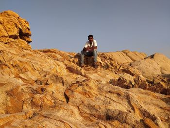 Man sitting on rock against sky