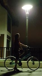 Woman with bicycle standing on illuminated railing at night