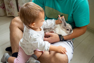 Midsection of father with baby and rabbit at home