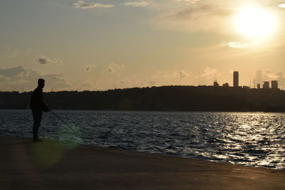 Silhouette man standing by sea against sky during sunset