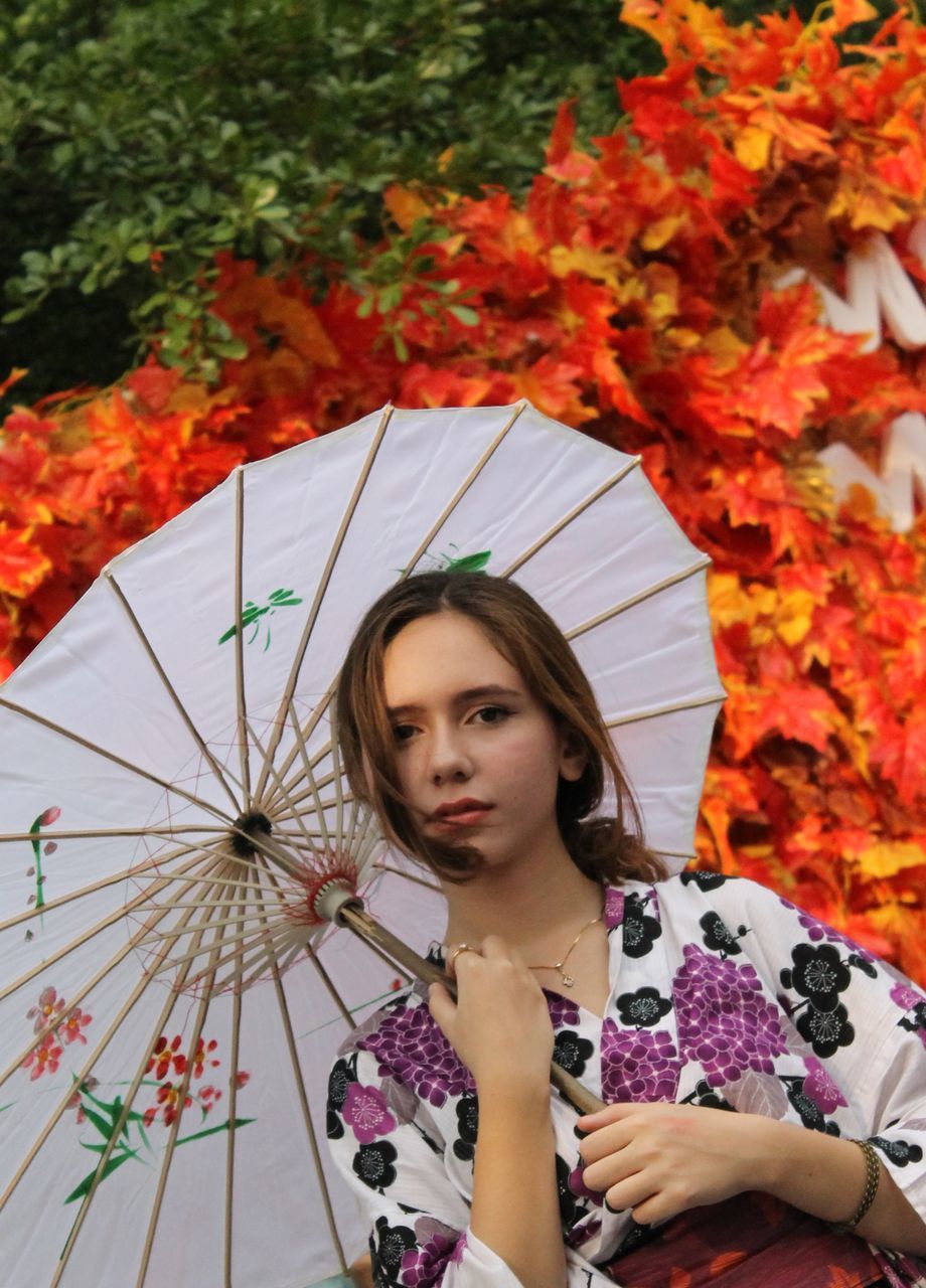 PORTRAIT OF BEAUTIFUL YOUNG WOMAN STANDING BY PLANTS