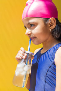 Side view of young woman drinking water against blue background