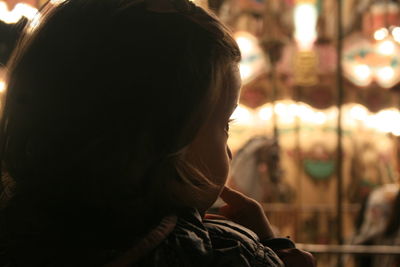 Rear view of baby girl looking away at illuminated amusement park during night