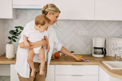 A young mother with a small boy cleans the kitchen at home, household chores on maternity leave