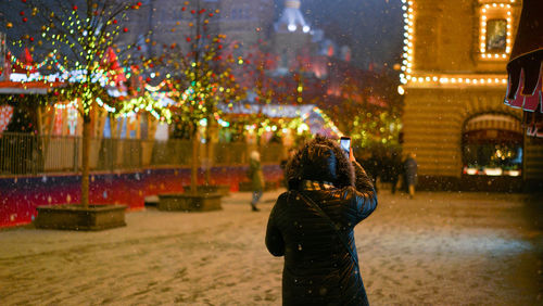 Rear view of man standing on illuminated street in city