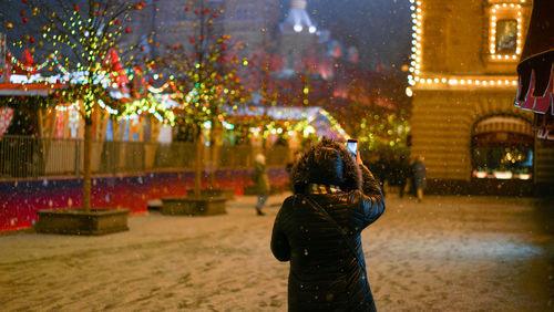 Rear view of woman standing on illuminated street in city during winter