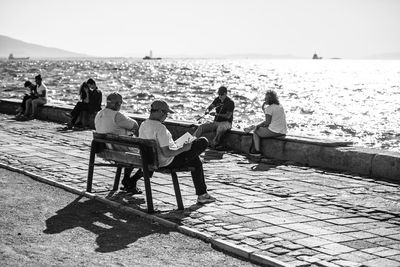 People sitting by sea against sky during sunny day
