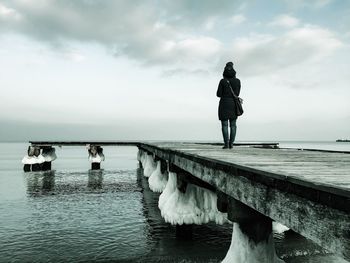 Rear view of woman standing on jetty in sea against sky