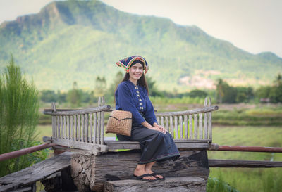 Portrait of smiling young woman sitting on floorboard against mountains