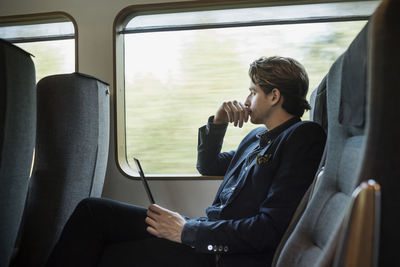 Side view of thoughtful businessman holding digital tablet in train