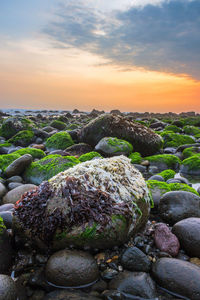 Rocks at sea shore against sky during sunset