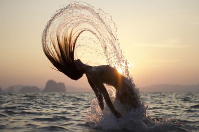 Mid section of woman splashing water against sky during sunset