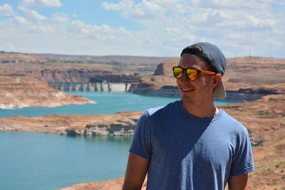 Smiling young man wearing sunglasses against lake