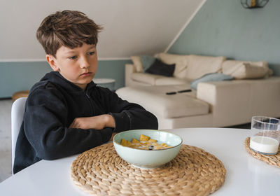 The boy sits over the plate and does not want to have a breakfast. no appetite.