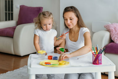 Mother and toddler daughter painting at home. happy creative family with child spending time