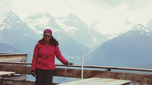 Woman standing by railing against snowcapped mountains