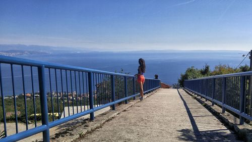 Woman standing on footbridge against sea