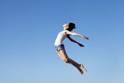Low angle view of woman jumping against clear blue sky