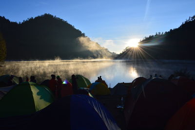 Group of people camping by lake in forest during sunset