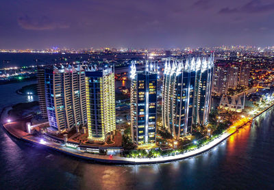 Illuminated buildings by river against sky at night