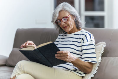 Senior woman wearing eyeglasses reading book at home