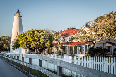 View of lighthouse by building against clear sky