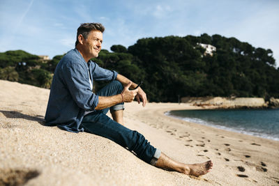 Man sitting on beach by sea against sky